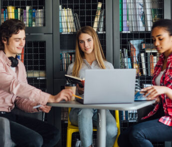 three-happy-students-writing-notebooks-laptop-library